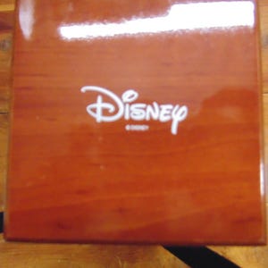 May include: A wooden box with a glossy finish and the word "Disney" printed in white on the top.