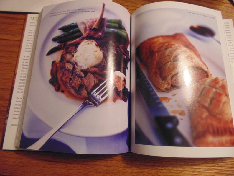May include: A cookbook spread featuring two plated dishes. One plate holds a grilled meat dish with asparagus and a dollop of white topping. The other shows a golden-brown pastry with a knife.
