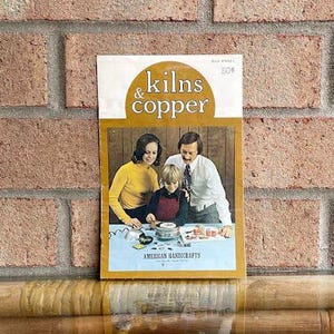 May include: A vintage instructional booklet titled Kilns & Copper featuring a cover illustration of a family working on a craft project. The booklet has a white and gold color scheme with the text American Handicrafts printed at the bottom.