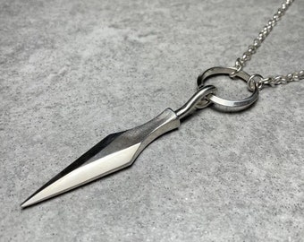 May include: A silver necklace with a sharp, pointed pendant shaped like a spearhead. The pendant is attached to a silver chain with a circular ring.