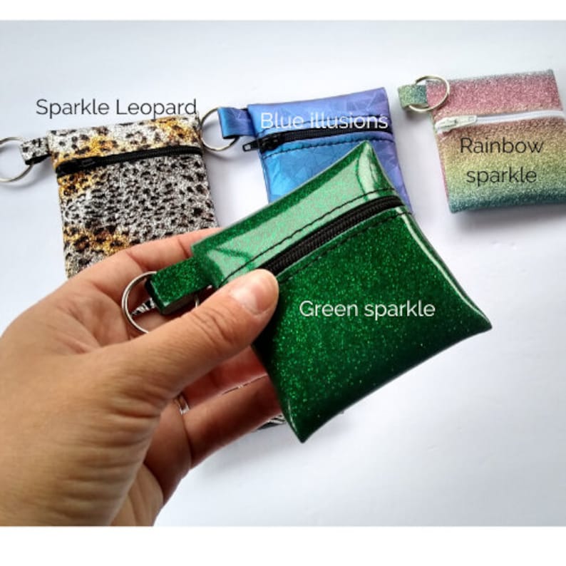 May include: Small, zippered coin purses in various colors and patterns. The purses include a green sparkle, blue illusion, rainbow sparkle, and sparkle leopard design. Each purse has a small loop with a metal ring attached.