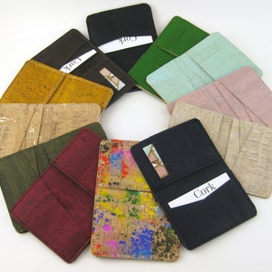 May include: A collection of cork card holders in various colors, including black, brown, green, and pink. Some holders feature a natural cork texture, while others have colorful paint splatters. Each holder has card slots and a small mirror.