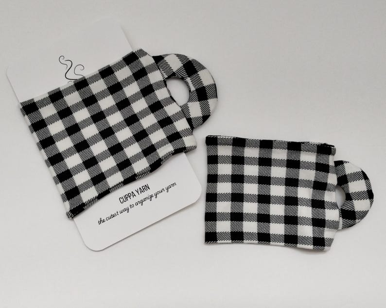 Może przedstawiać: Dwa czarne i białe ginghamowe pojemniki na wł&oacute;czkę. Pojemniki mają kształt kubk&oacute;w z uchwytem. Tekst "CUPPA YARN the cutest way to organize your yarn" jest nadrukowany na białej kartce za pojemnikami.