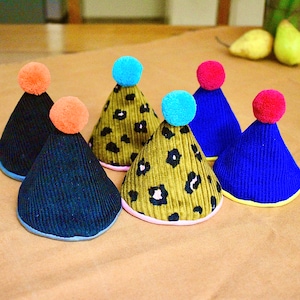 Puede incluir: Cinco sombreros de fiesta coloridos hechos de tela de pana. Los sombreros son de varios colores, incluyendo azul, verde y negro. Los sombreros tienen diferentes patrones, incluyendo estampado de leopardo y colores sólidos.