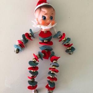 May include: A vintage Christmas elf ornament with a felt body and a plastic head. The elf's body is made of red and green felt circles strung together with gold beads. The elf has a white felt collar and a red felt hat.