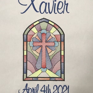 May include: Embroidered white fabric with a stained glass window design featuring a red cross. The text "Xavier" and "April 4th 2021" is embroidered in blue.