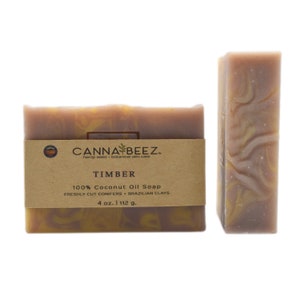 May include: Two bars of Timber soap with a brown paper label. The label reads "CANNA BEEZ" and "100% Coconut Oil Soap". The soap is a mix of brown and yellow tones, with a marbled appearance. The label also states the soap is 4 oz. or 112 g.