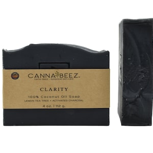 May include: A black bar of soap with a brown label that reads "CANNA BEEZ. hemp seed botanical skin care CLARITY 100% Coconut Oil Soap LEMON TEA TREE ACTIVATED CHARCOAL 4 oz. | 112 g."