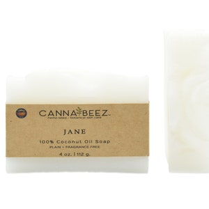 以下が含まれることがあります： 茶色の紙のラベルが付いた白いココナッツオイル石鹸のバーが2本。ラベルには「CANNA BEEZ. hemp seed botanical skin care JANE 100% Coconut Oil Soap PLAIN + FRAGRANCE FREE 4 oz. 112 g.」と書いてあります。