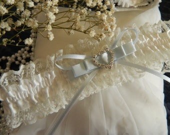 May include: White lace garter with a satin bow and a rhinestone heart charm. The garter is tied with a light blue ribbon.