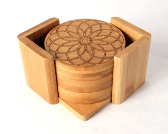 May include: A set of six round bamboo coasters with a geometric design. The coasters are stacked in a wooden holder.