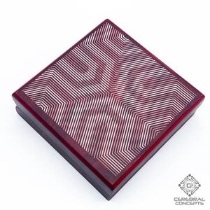 May include: Square, dark red wooden box with a geometric pattern on the lid. The pattern consists of white lines arranged in a starburst design. The box is viewed from a high angle against a white background.