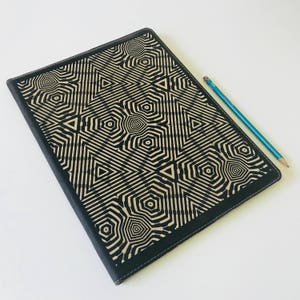 May include: Black leather folder with a geometric pattern in beige. The pattern is made up of triangles and hexagons.
