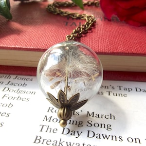 Real dandelion seeds inside a glass sphere strung from a long chain to create a striking necklace.