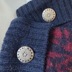 Puede incluir: Primer plano de un su&eacute;ter de punto azul marino con dos botones plateados. Los botones tienen un dise&ntilde;o decorativo de estrella. El su&eacute;ter tiene un patr&oacute;n rojo y burdeos en la parte inferior derecha.