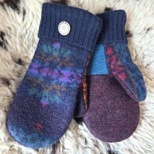 Puede incluir: Un par de mitones hechos a mano en tonos azul marino, morado y verde azulado. Los mitones presentan un dise&ntilde;o estampado en la parte delantera y un color morado liso en las palmas. Los pu&ntilde;os son de color azul marino con un bot&oacute;n decorativo.