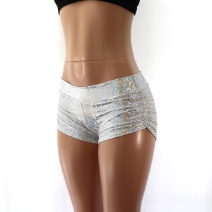 Op de afbeelding: Zilveren holografische shorts met een hoge taille en een subtiel gestructureerd patroon. Het kledingstuk heeft een nauwsluitend silhouet met geplooide details aan de zijkanten langs de buitenkant van de dijen voor een rimpelend effect.