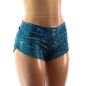 May include: Teal high-waisted shorts with a textured, shimmering fabric. The shorts are ruched at the sides and have a low-cut leg opening. The garment is displayed on a mannequin.