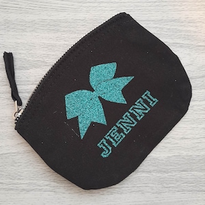 Può includere: Borsa a zip in tela nera con un fiocco di glitter turchese e il nome "JENNI" stampato in glitter turchese.