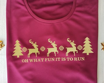 Puede incluir: Camiseta color burdeos con un diseño dorado de renos y árboles de Navidad. El texto "Oh what fun it is to run" está impreso debajo del diseño.