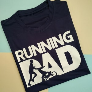 Könnte beinhalten: Ein marineblaues T-Shirt mit dem Text "RUNNING DAD" in Weiß. Unter dem Text befindet sich eine Silhouette einer Person, die mit einem Kinderwagen läuft.