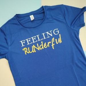 Pode incluir: Uma camiseta azul royal com o texto "Feeling Runderful" impresso em branco e amarelo.
