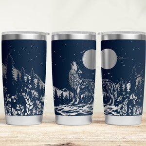 May include: Navy blue insulated tumbler with a silver wolf howling at the moon design. The tumbler features a forest scene with trees, mountains, and stars. The tumbler has a silver lid and a white base.