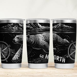 以下が含まれることがあります： 黒と白のデザインのステンレス鋼製トラベルマグ3個。デザインは、水中で泳ぐクマ、コンパス、山、そして「GO NORTH」という言葉が特徴です。マグカップはシルバーのリムとベースが付いています。
