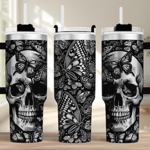 May include: A black and white tumbler featuring a skull design with butterflies. The tumbler has a black handle, a white straw, and a silver lid. The design is repeated on all sides of the tumbler.