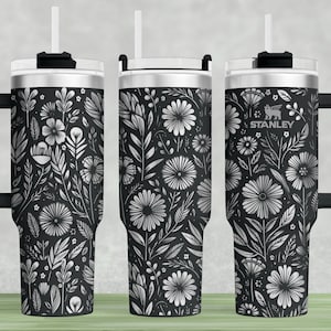 Puede incluir: Tres vasos de acero inoxidable con tapas y asas negras. Cada vaso presenta un patr&oacute;n floral en blanco y negro. El vaso del centro tiene la palabra "STANLEY" impresa.