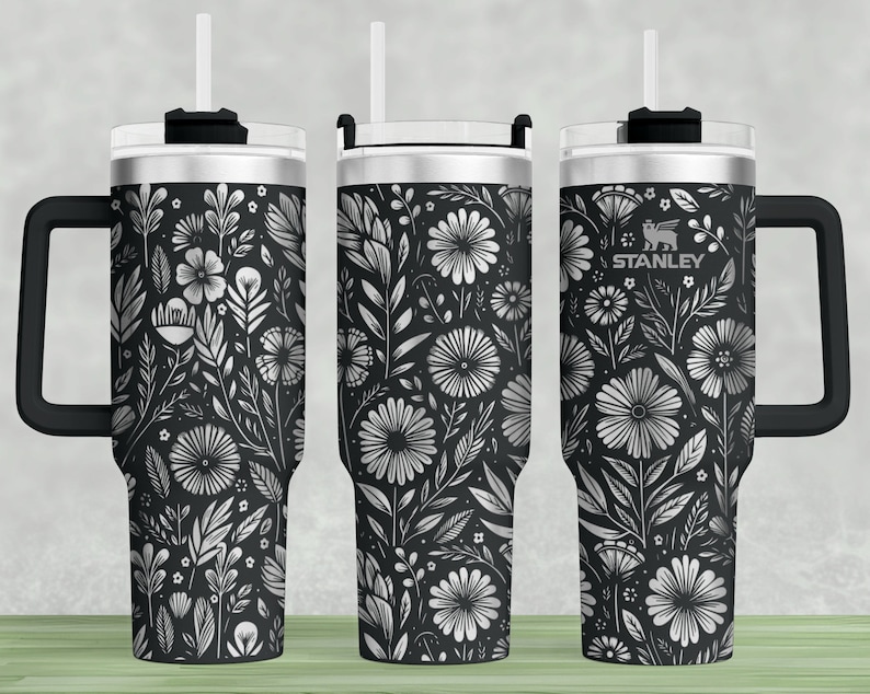 Puede incluir: Tres vasos de acero inoxidable con tapas y asas negras. Cada vaso presenta un patr&oacute;n floral en blanco y negro. El vaso del centro tiene la palabra "STANLEY" impresa.