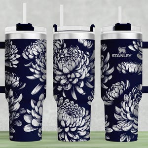 May include: A navy blue stainless steel tumbler with a white floral pattern and a black handle. The tumbler has a lid with a straw hole and the word "STANLEY" is printed on the side.