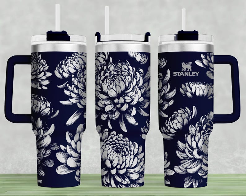 May include: A navy blue stainless steel tumbler with a white floral pattern and a black handle. The tumbler has a lid with a straw hole and the word "STANLEY" is printed on the side.