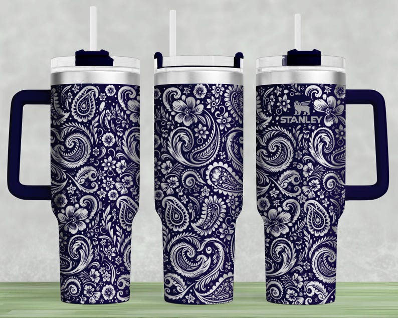 May include: A navy blue insulated tumbler with a white paisley floral design. The tumbler has a handle, a clear lid, and a white straw. The Stanley logo is visible on the side.
