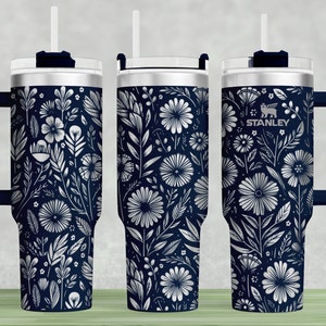 Puede incluir: Un vaso de acero inoxidable con un patr&oacute;n floral azul marino y un asa negra. El vaso tiene una tapa con un agujero para pajita y la palabra "STANLEY" est&aacute; impresa en el lateral.