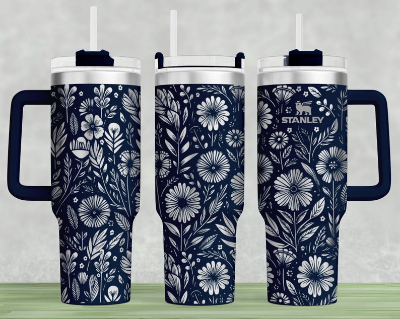 Puede incluir: Un vaso de acero inoxidable con un patr&oacute;n floral azul marino y un asa negra. El vaso tiene una tapa con un agujero para pajita y la palabra "STANLEY" est&aacute; impresa en el lateral.