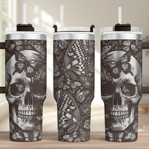 May include: A stainless steel tumbler with a black and white butterfly and skull design. The tumbler has a handle, a lid, and a straw. The design features a detailed skull surrounded by butterflies. The tumbler is suitable for cold and hot beverages.