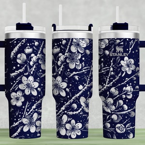 May include: A stainless steel tumbler with a navy blue and white floral design. The tumbler has a lid with a straw hole and a handle. The tumbler is branded with the Stanley logo.