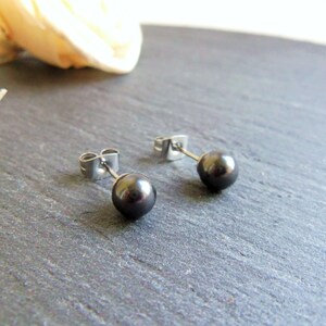 Peut inclure: Une paire de boucles d'oreilles en perles noires avec des tiges argentées. Les boucles d'oreilles sont sur une surface gris foncé.