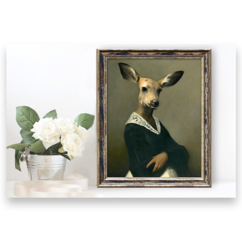 May include: A framed painting of a deer with a human-like face wearing a dark green dress and a white lace collar. The painting has a gold frame and is set against a white background.