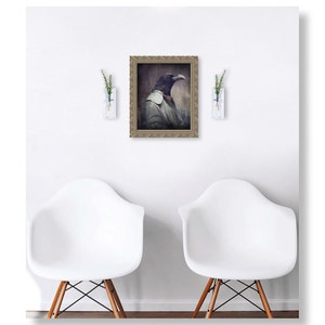 Puede incluir: Un retrato enmarcado de un cuervo con una camisa blanca y una corbata de lazo roja. El cuervo mira hacia la derecha. El retrato est&aacute; colgado en una pared blanca entre dos jarrones blancos con plantas verdes.