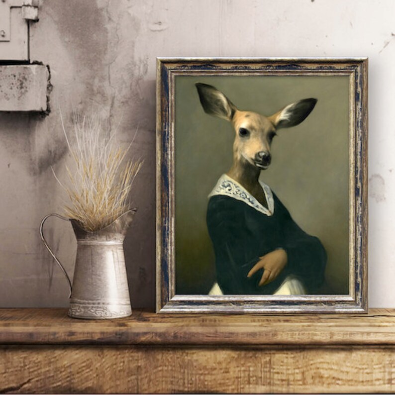 May include: A framed painting of a deer with a human-like face wearing a dark green dress with a white lace collar. The painting has a gold frame and is set against a light brown wall.