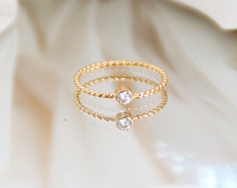 May include: A delicate gold ring with a twisted band and a single, clear gemstone.
