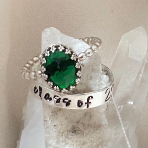 May include: A silver ring with a green gemstone and the inscription "Class of 20" on the band.
