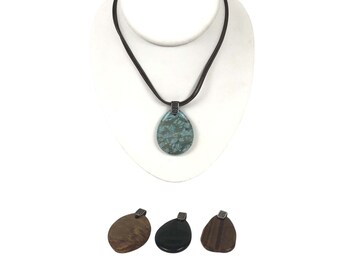 May include: A brown leather cord necklace with a teardrop-shaped pendant. The pendant is made of a blue and green stone with a silver-toned metal accent. The necklace is displayed on a white mannequin bust. Three additional pendants are shown below the necklace: one brown, one black, and one brown with a wood grain pattern.
