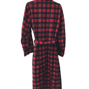 May include: A long-sleeved robe featuring a vibrant red and dark navy blue plaid pattern. The garment includes a matching fabric belt tied at the waist, a folded collar, and a straight hemline that extends to the lower calf area of the robe.
