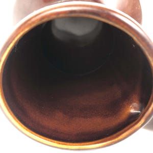 May include: Close-up of a brown ceramic mug, showing the inside and rim. The mug has a glossy finish with a dark brown interior and a lighter brown exterior. The handle is visible on the right.