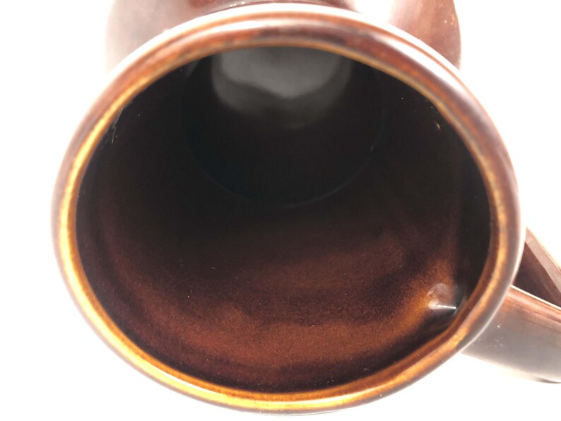 May include: Close-up of a brown ceramic mug, showing the inside and rim. The mug has a glossy finish with a dark brown interior and a lighter brown exterior. The handle is visible on the right.