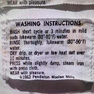 May include: A white fabric garment tag with black text reading WASHING INSTRUCTIONS, WASH short cycle or 3 minutes in mild suds lukewarm (80-90 F) water, RINSE thoroughly, lukewarm (80-90 F) water, DRY drip, or dryer on low heat, PRESS, WEAR with pleasure, 1962 Pendleton Woolen Mills.