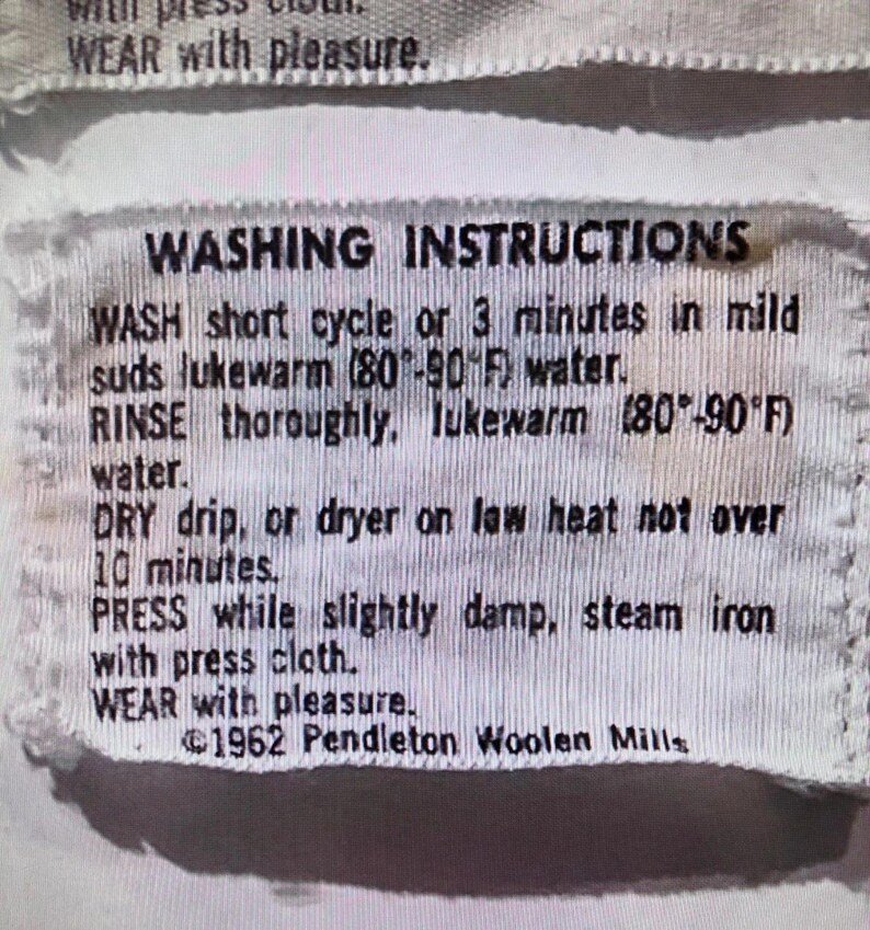 May include: A white fabric garment tag with black text reading WASHING INSTRUCTIONS, WASH short cycle or 3 minutes in mild suds lukewarm (80-90 F) water, RINSE thoroughly, lukewarm (80-90 F) water, DRY drip, or dryer on low heat, PRESS, WEAR with pleasure, 1962 Pendleton Woolen Mills.